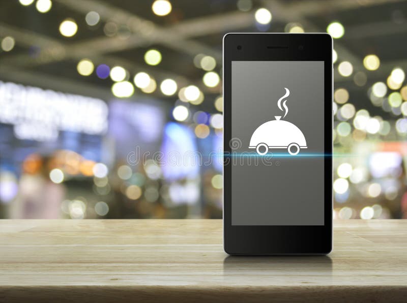 Food delivery concept. Restaurant cloche flat icon on modern smart phone screen on wooden table over blur light and shadow of shopping mall, Food delivery royalty free stock image Food delivery concept. Restaurant cloche flat icon on modern smart phone screen on wooden table over blur light and shadow of shopping mall, Food delivery royalty free stock image