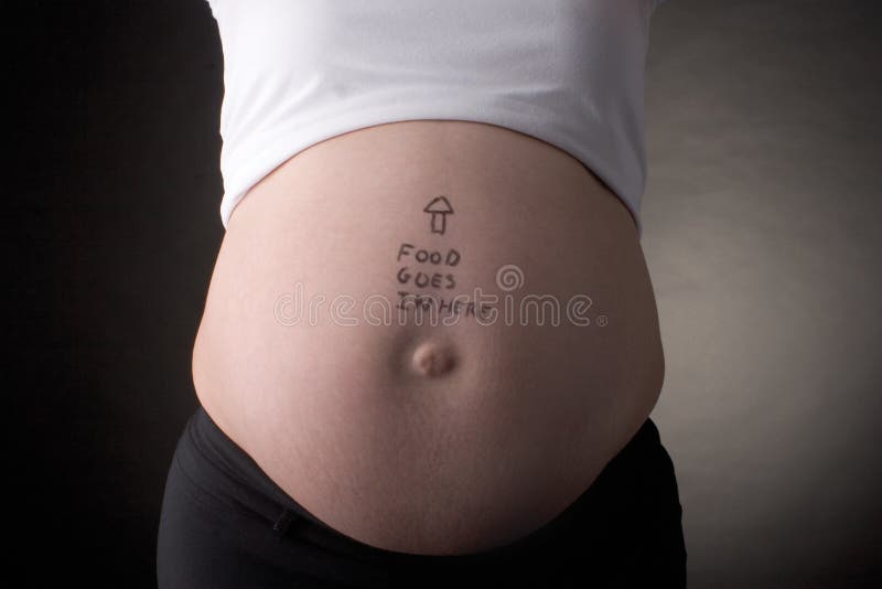 Seven month pregnant belly with arrow pointing up and food goes in here written on the stomach. Seven month pregnant belly with arrow pointing up and food goes in here written on the stomach