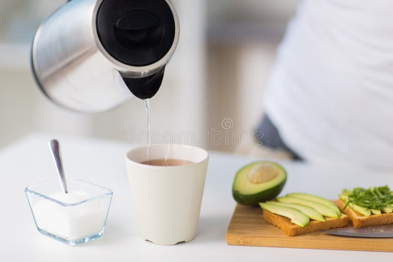 Ceainic turnând apă caldă în ceașca de ceai la domiciliu stock image
