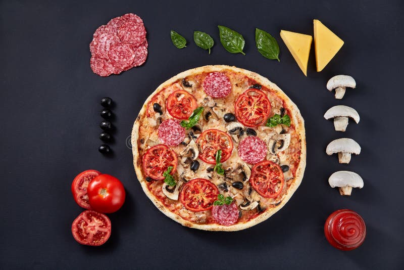 Food ingredients and spices for cooking and delicious italian pizza on black concrete background.