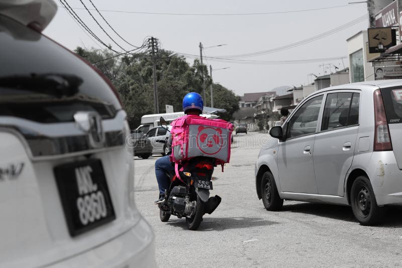 A Foodpanda courier delivery Malay man in the suburbs of Ipoh streets, Malaysia. Focus has been placed on him by desaturating the colours around him. A Foodpanda courier delivery Malay man in the suburbs of Ipoh streets, Malaysia. Focus has been placed on him by desaturating the colours around him