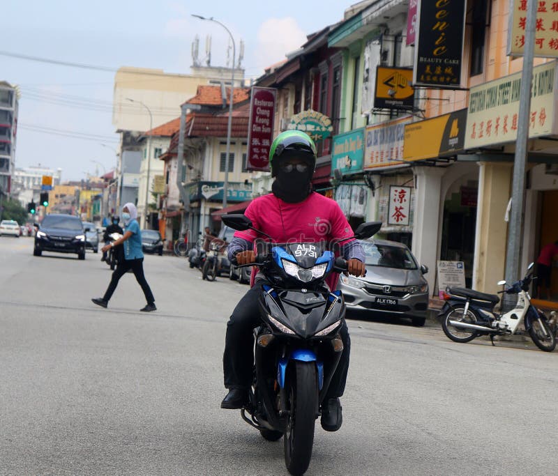 FoodPanda delivery rider out on the road in Ipoh city, Malaysia. His face is all covered up except for his eyes. A Malay woman who is crossing the road and another motorcyclist can be seen donning a face mask due to the Covid-19 pandemic. This picture was taken during the `recovery movement control order` or RMCO period in Malaysia. FoodPanda delivery rider out on the road in Ipoh city, Malaysia. His face is all covered up except for his eyes. A Malay woman who is crossing the road and another motorcyclist can be seen donning a face mask due to the Covid-19 pandemic. This picture was taken during the `recovery movement control order` or RMCO period in Malaysia