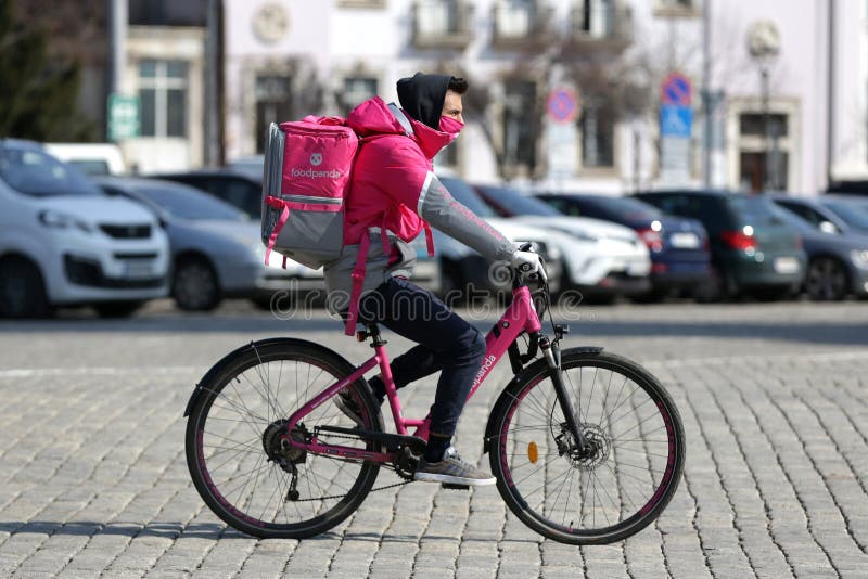 Sofia, Bulgaria - 30 March, 2020: A worker at Foodpanda online food delivery company rides a bicycle with food to an address. Wearing a protective face mask during the Coronavirus disease COVID-19 outbreak epidemic. Sofia, Bulgaria - 30 March, 2020: A worker at Foodpanda online food delivery company rides a bicycle with food to an address. Wearing a protective face mask during the Coronavirus disease COVID-19 outbreak epidemic