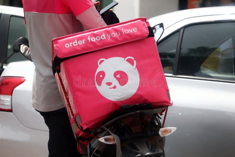 Foodpanda delivery rider standing at the side of his motorbike while checking out his smartphone in Malaysia. Note the updated Foodpanda logo on the delivery container thermobag. Foodpanda delivery rider standing at the side of his motorbike while checking out his smartphone in Malaysia. Note the updated Foodpanda logo on the delivery container thermobag