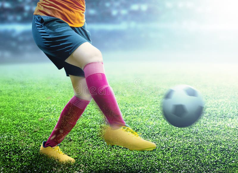 Football player woman in orange jersey kicking the ball on the football field