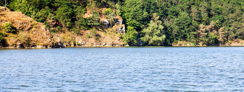 The foreground of a large river with waves, windy weather. Opposite river bank with rocks and trees. Panorama summer. Nature wilderness landscape royalty free stock photos The foreground of a large river with waves, windy weather. Opposite river bank with rocks and trees. Panorama summer. Nature wilderness landscape royalty free stock photos
