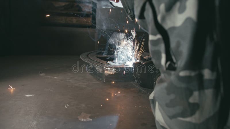 Forge Workshop. Smithy. Worker in a Welding Hood Helmet Welds a Part by