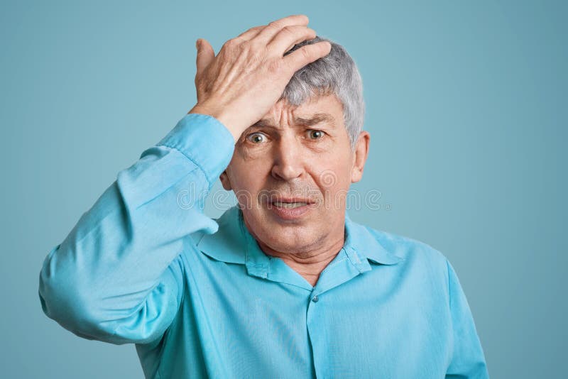 Forgetful handsome elederly wrinkled man in blue shirt, keeps hand on head, feels desperately as forgets about important meeting, royalty free stock photo Forgetful handsome elederly wrinkled man in blue shirt, keeps hand on head, feels desperately as forgets about important meeting, royalty free stock photo