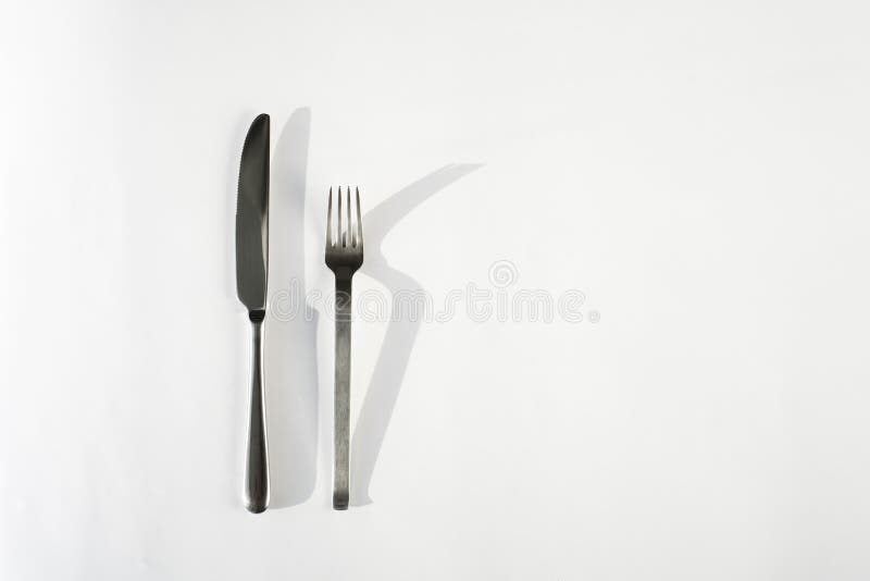 Fork and knife on a white background with hard shadows from the sun`s rays. top view close-up. cutlery. Subject photography.