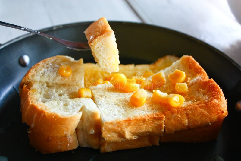A fork spreading butter and corn on toast