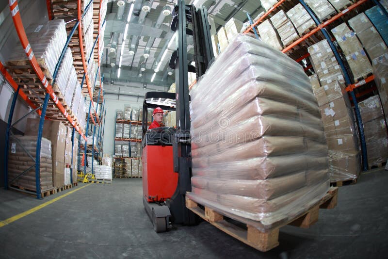 Forklift driver in uniforme rossa e casco al lavoro in magazzino lente occhio di pesce.