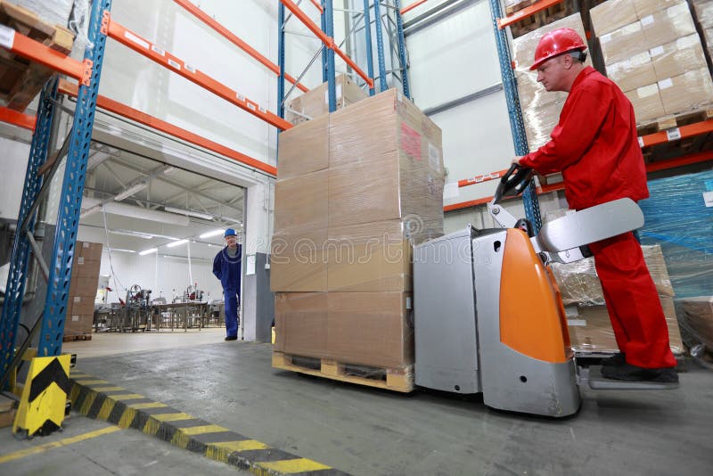 Forklift loader with cardboard freight moving in storehouse,another worker watching him