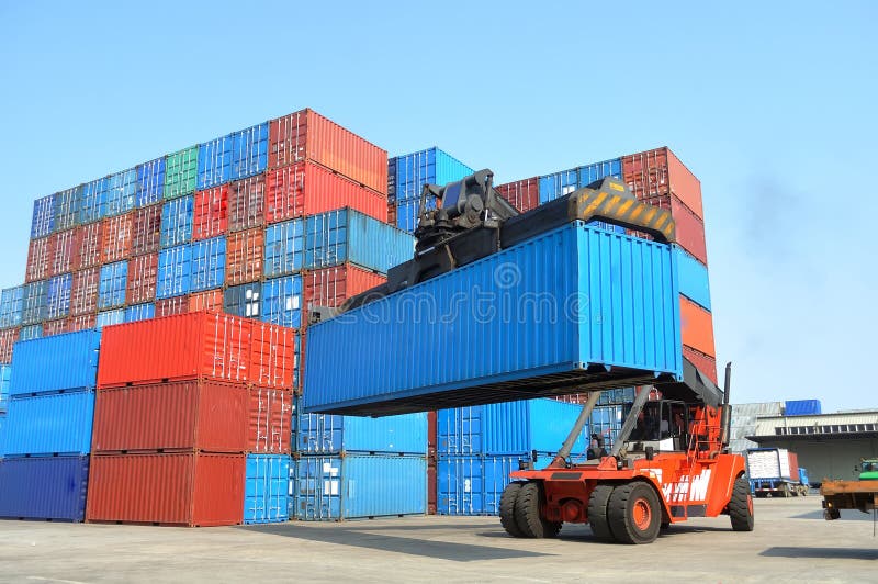 A forklift crane parked next to stacks of containers. A forklift crane parked next to stacks of containers