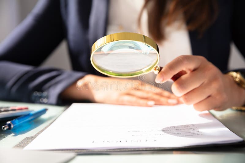 Close-up Of A Businesswoman`s Hand Looking At Contract Form Through Magnifying Glass. Close-up Of A Businesswoman`s Hand Looking At Contract Form Through Magnifying Glass
