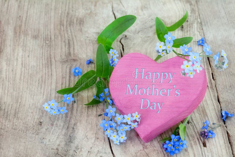 Pink heart shape made of wood with forget-me-not flowers on a rustic wooden background and text happy mothers day. Pink heart shape made of wood with forget-me-not flowers on a rustic wooden background and text happy mothers day