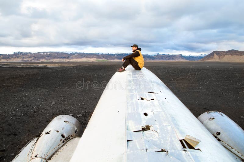 Forme al individuo que se sienta en un avión que se estrelló en la playa negra o foto de archivo Forme al individuo que se sienta en un avión que se estrelló en la playa negra o foto de archivo
