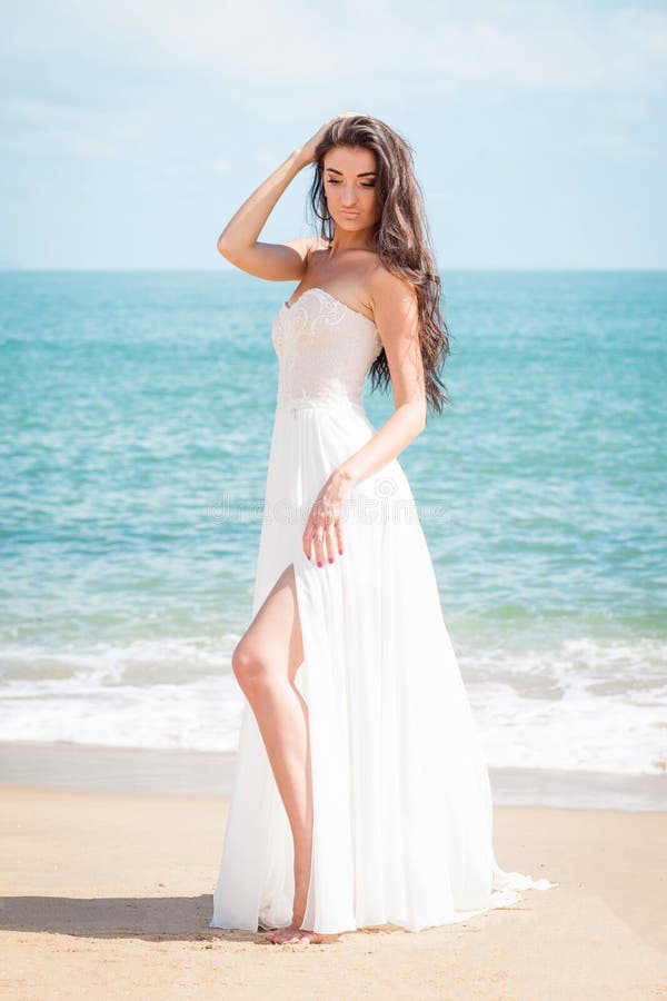 Forme a noiva que anda abaixo da praia em um vestido branco A menina bonita anda pena descalça a praia foto de stock royalty free Forme a noiva que anda abaixo da praia em um vestido branco A menina bonita anda pena descalça a praia foto de stock royalty free