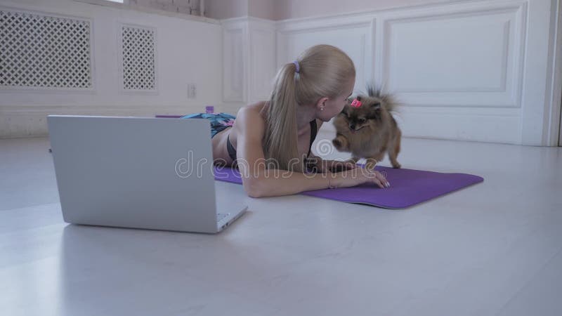 Forme physique à la maison Jeune femme pendant l'exercice et jeux avec le petit Spitz de chien Vidéos de observation sur l'Intern