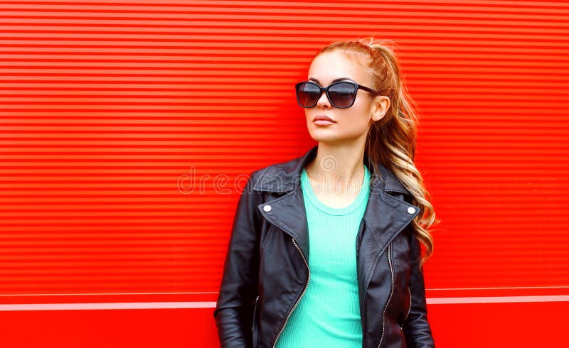 Forme a retrato la mujer hermosa en chaqueta negra de la roca de las gafas de sol sobre rojo fotos de archivo Forme a retrato la mujer hermosa en chaqueta negra de la roca de las gafas de sol sobre rojo fotos de archivo