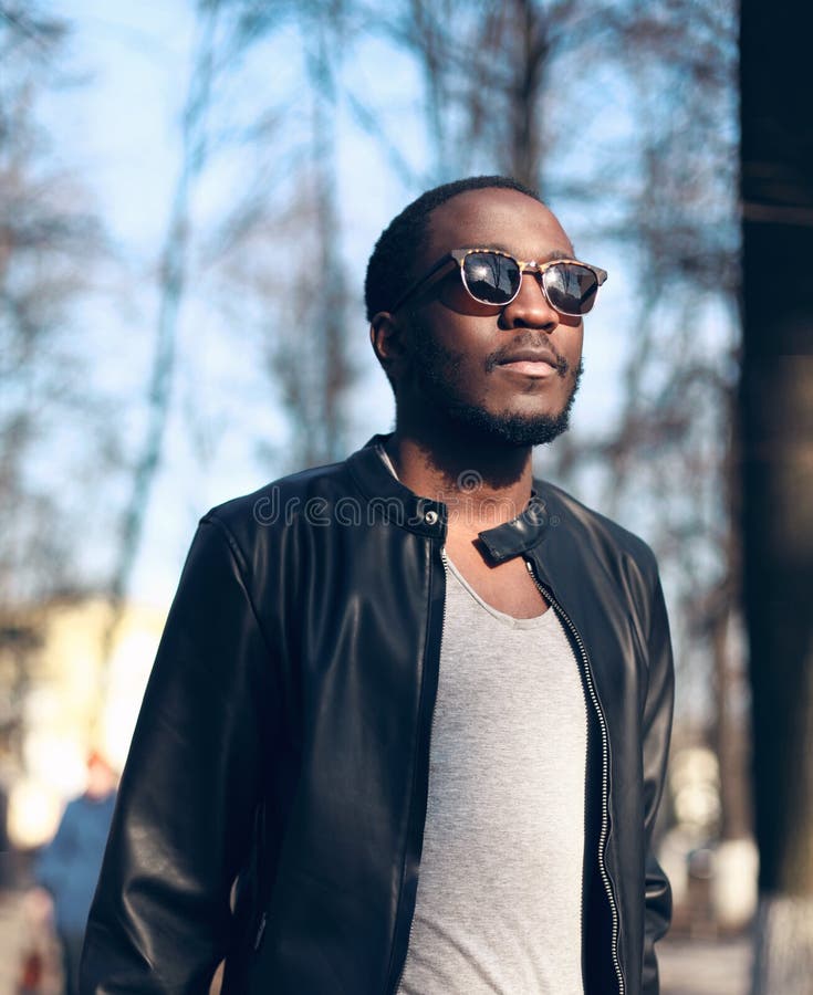 Forme a retrato las gafas de sol que llevan del hombre africano, chaqueta de cuero negra de roca en la calle foto de archivo libre de regalías Forme a retrato las gafas de sol que llevan del hombre africano, chaqueta de cuero negra de roca en la calle foto de archivo libre de regalías