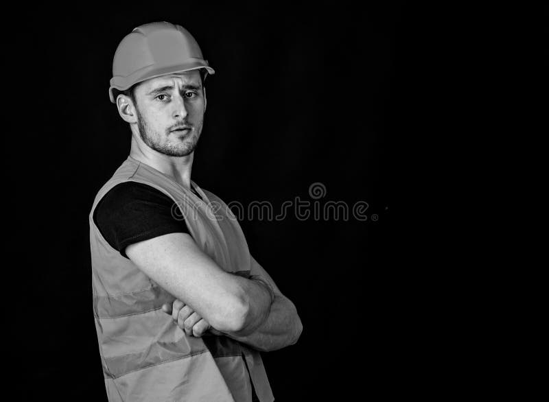 Forte concetto del costruttore L'uomo in casco, armi della tenuta del casco ha attraversato sul petto, fondo nero Lavoratore, app fotografie stock Forte concetto del costruttore L'uomo in casco, armi della tenuta del casco ha attraversato sul petto, fondo nero Lavoratore, app fotografie stock
