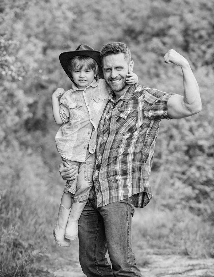 Forti padre e figlio in cappello da cowboy sul ranch bambino in stivali di gomma Pap? felice dell'uomo in essere umano e natura d immagini stock libere da diritti Forti padre e figlio in cappello da cowboy sul ranch bambino in stivali di gomma Pap? felice dell'uomo in essere umano e natura d immagini stock libere da diritti