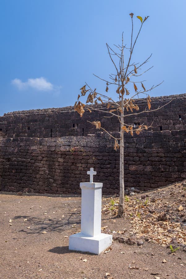 Fortress wall, tree and small white column with cross and without inscriptions in 19th century Fort Cabo de Rama in India
