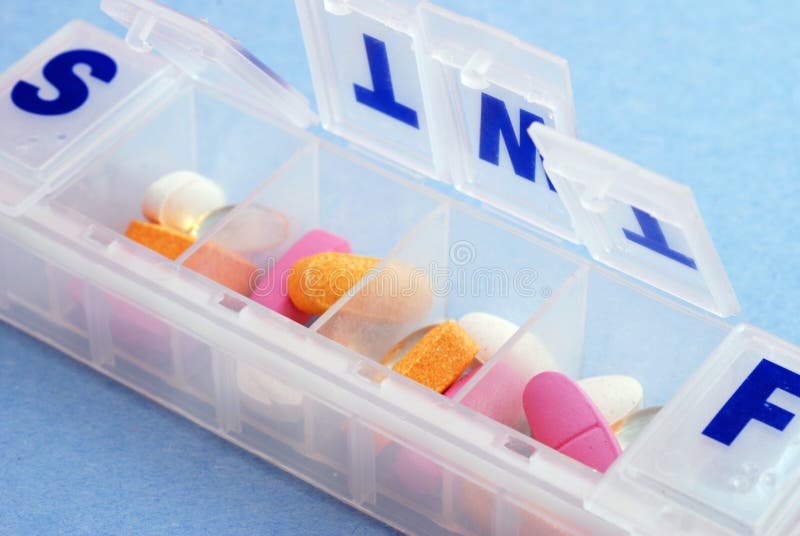 A pillbox with mutli colored pills and vitamins against a blue background. A pillbox with mutli colored pills and vitamins against a blue background