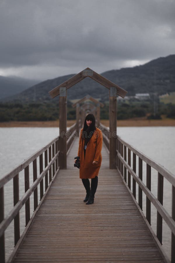 Fot?grafo moreno de la mujer con la trenca anaranjada en un puente foto de archivo Fot?grafo moreno de la mujer con la trenca anaranjada en un puente foto de archivo
