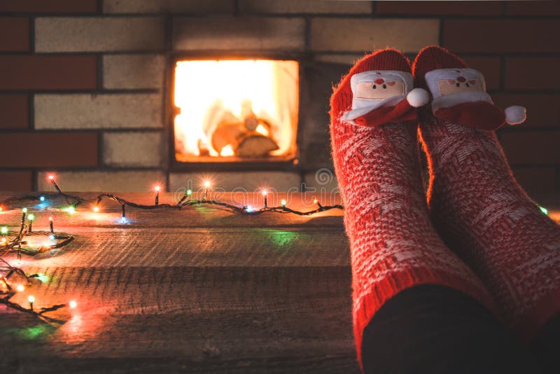 Fot i röda sockor vid spisen Kopplar av, genom varmt brand och att värma hennes fot i julsockor upp Santa Claus och rött klumpa i royaltyfria bilder Fot i röda sockor vid spisen Kopplar av, genom varmt brand och att värma hennes fot i julsockor upp Santa Claus och rött klumpa i royaltyfria bilder
