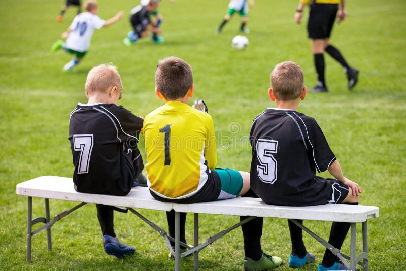 Fotbollfotbollbänk Unga fotbollsspelare som sitter på fotbollersättningbänk