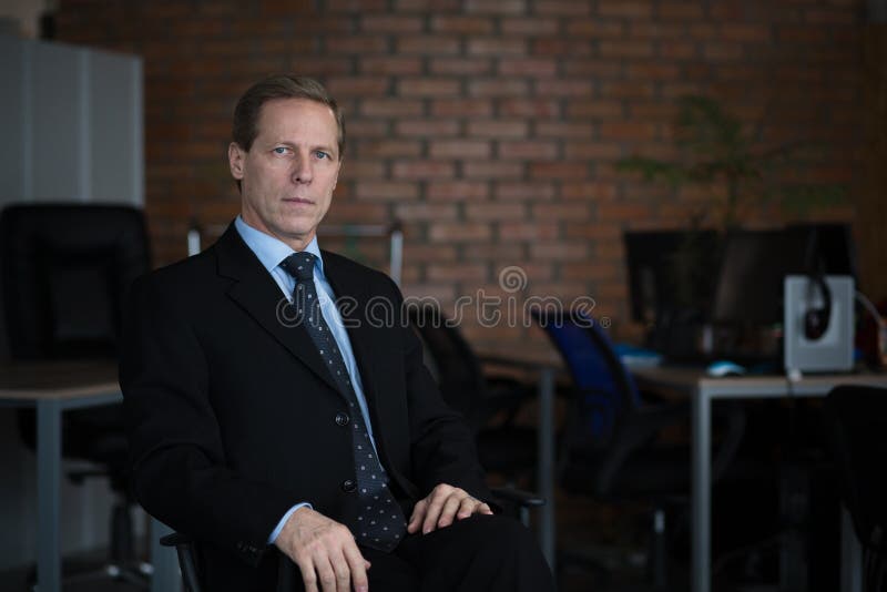 Foto ascendente próxima do businessma atrativo em um terno preto que senta-se na cadeira foto de stock Foto ascendente próxima do businessma atrativo em um terno preto que senta-se na cadeira foto de stock