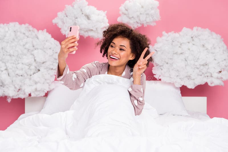 Photo of dreamy sweet lady wear pajama lying bed recording video modern device showing v-sign isolated pink color background. Photo of dreamy sweet lady wear pajama lying bed recording video modern device showing v-sign isolated pink color background.