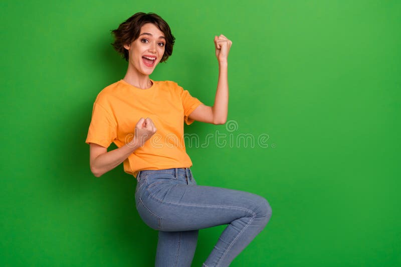 Foto av en ung kvinna med stor entusiasm och klädd orange tshirt med stigande fiber på tomt utrymme med isolerad grön bakgrund arkivfoton