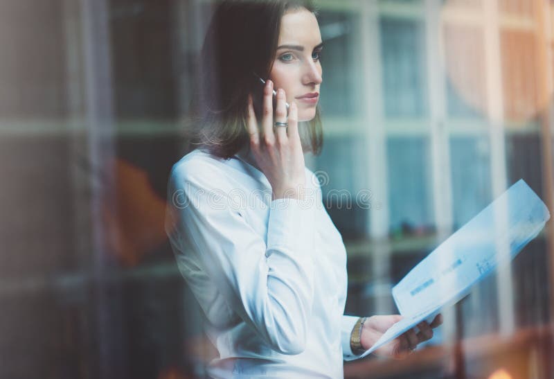 Foto bedrijfsvrouw die wit overhemd dragen, smartphone spreken en documenten in handen houden Het bureau van de open plekzolder P stock foto's Foto bedrijfsvrouw die wit overhemd dragen, smartphone spreken en documenten in handen houden Het bureau van de open plekzolder P stock foto's