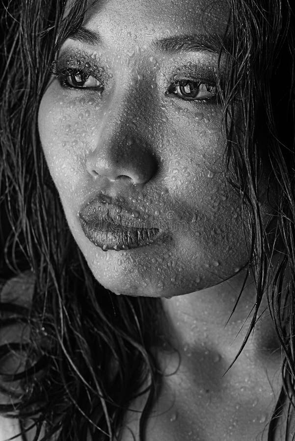 Black and white photo of Asian model with wet hair and drops of water on face. Photo in studio. Black and white photo of Asian model with wet hair and drops of water on face. Photo in studio