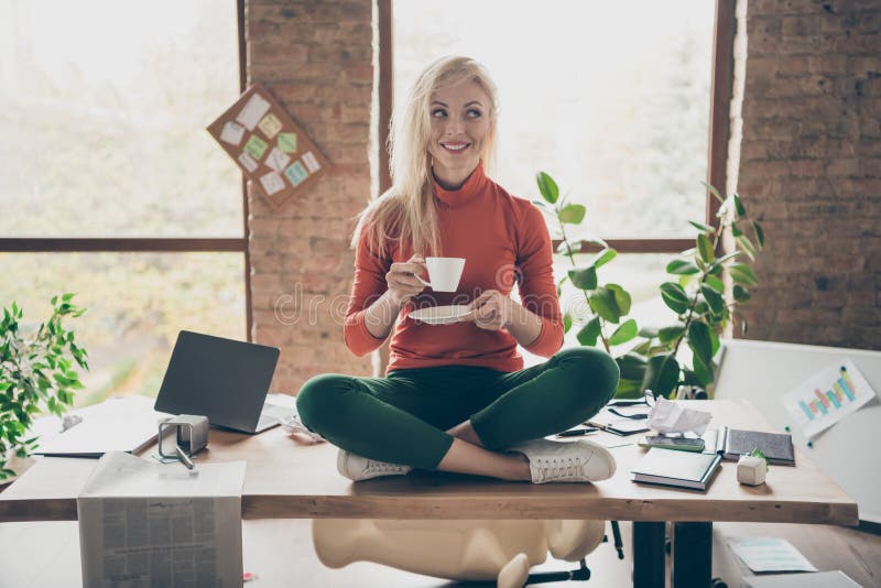 Foto completa del corpo di una donna felice e positiva proprietaria di un'azienda seduta su un tavolo per le gambe incrociate rip