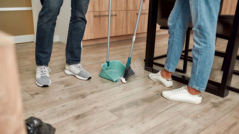 Foto cortada de casal com roupas casuais varrendo o chão enquanto limpavam a cozinha moderna juntos imagens de stock royalty free