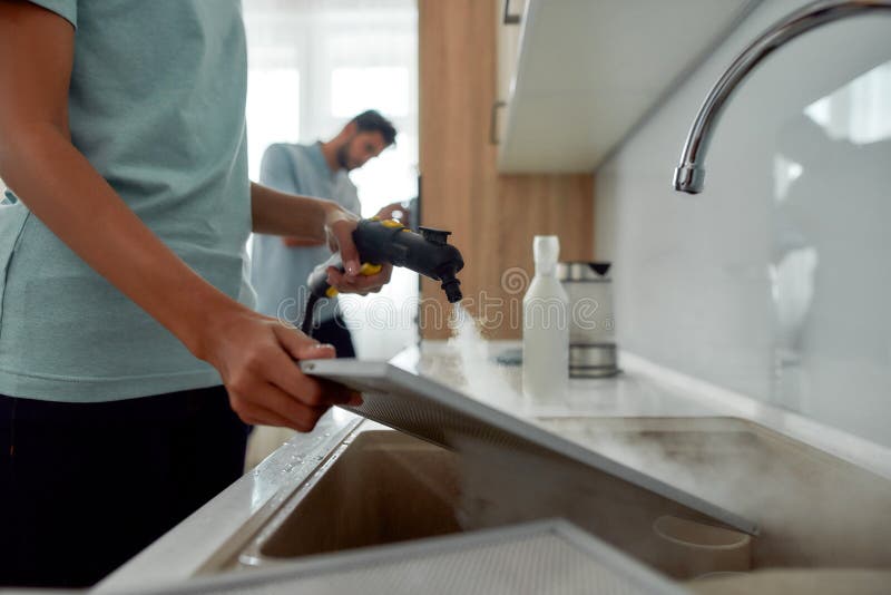 Foto cortada de uma mulher em filtros uniformes de limpeza para a cozinha com limpeza a vapor enquanto seu colega macho imagem de stock