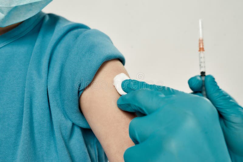 Foto cortada do médico em luvas estéreis azuis injetando-se em braço a um garotinho usando máscara médica. foco em fotografia de stock