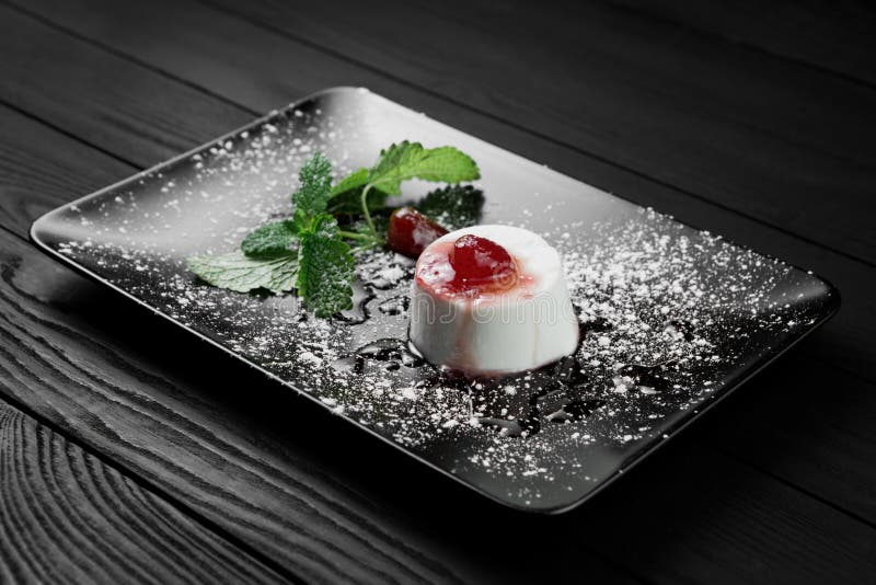 A foto da sobremesa italiana do cotta do panna com melaço da morango e a hortelã folheiam no fundo de madeira preto foto de stock royalty free A foto da sobremesa italiana do cotta do panna com melaço da morango e a hortelã folheiam no fundo de madeira preto foto de stock royalty free