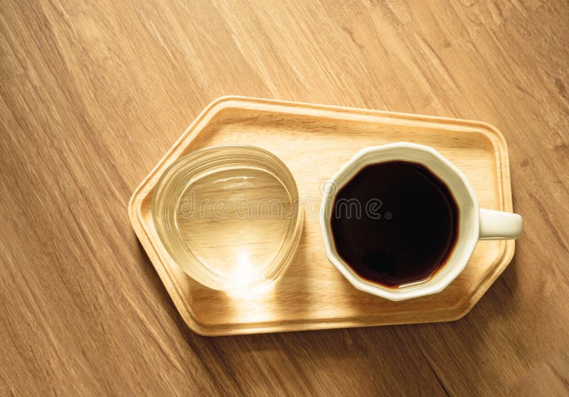 Foto da vista superior, um copo branco do café preto do americano e um vidro da água mineral na bandeja de madeira na textura de foto de stock Foto da vista superior, um copo branco do café preto do americano e um vidro da água mineral na bandeja de madeira na textura de foto de stock
