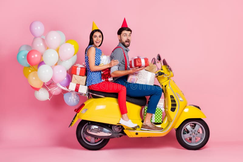 Full length photo crazy positive energetic two people buddies drive, yellow retro motor bike hold gift boxes have air balloons fly wear cone shirt red trousers isolated pink color background. Full length photo crazy positive energetic two people buddies drive, yellow retro motor bike hold gift boxes have air balloons fly wear cone shirt red trousers isolated pink color background