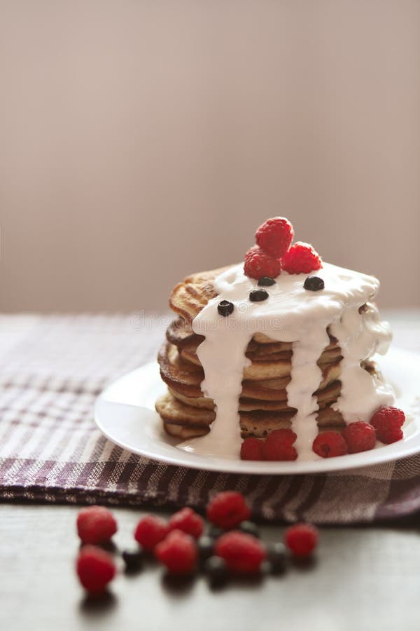 Foto de crepes hechas en casa con crema agria, frambuesas y arándanos en la placa blanca en la toalla marrón del algodón en rústi fotos de archivo libres de regalías Foto de crepes hechas en casa con crema agria, frambuesas y arándanos en la placa blanca en la toalla marrón del algodón en rústi fotos de archivo libres de regalías