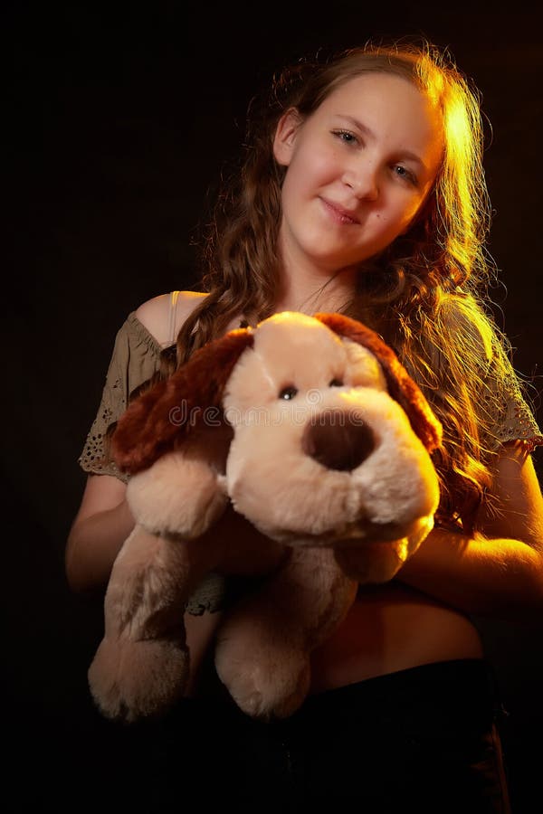 Foto de estudio de una joven adolescente con su juguete de perro suave en las manos. modelo posando sobre fondo negro imágenes de archivo libres de regalías