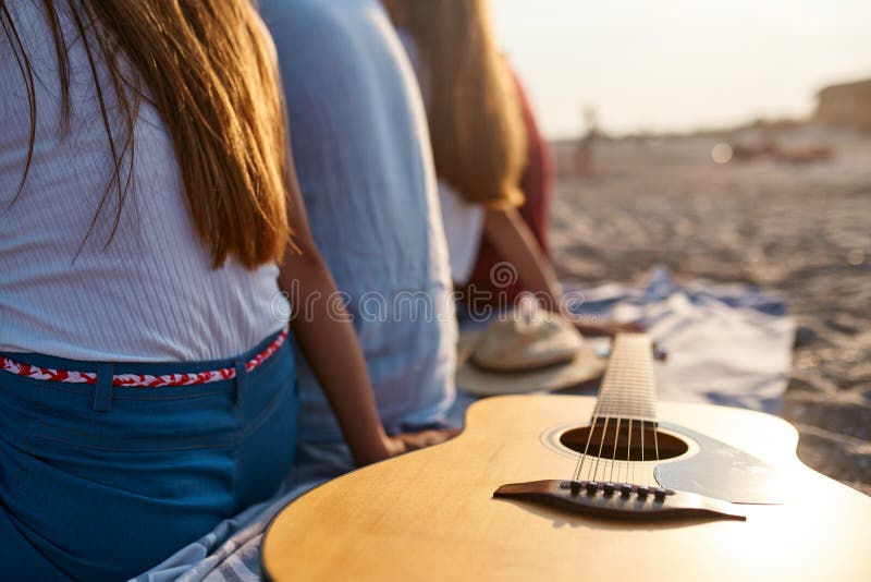 foto de la guitarra ac?stica de madera en la toalla de playa Opini?n trasera el grupo de amigos que se sientan junto en la arena imagen de archivo libre de regalías foto de la guitarra ac?stica de madera en la toalla de playa Opini?n trasera el grupo de amigos que se sientan junto en la arena imagen de archivo libre de regalías