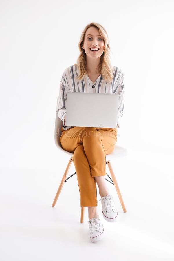 Foto de la mujer linda cauc?sica que lleva la ropa casual que sonr?e en la c?mara y que usa el ordenador port?til mientras que se imagen de archivo Foto de la mujer linda cauc?sica que lleva la ropa casual que sonr?e en la c?mara y que usa el ordenador port?til mientras que se imagen de archivo