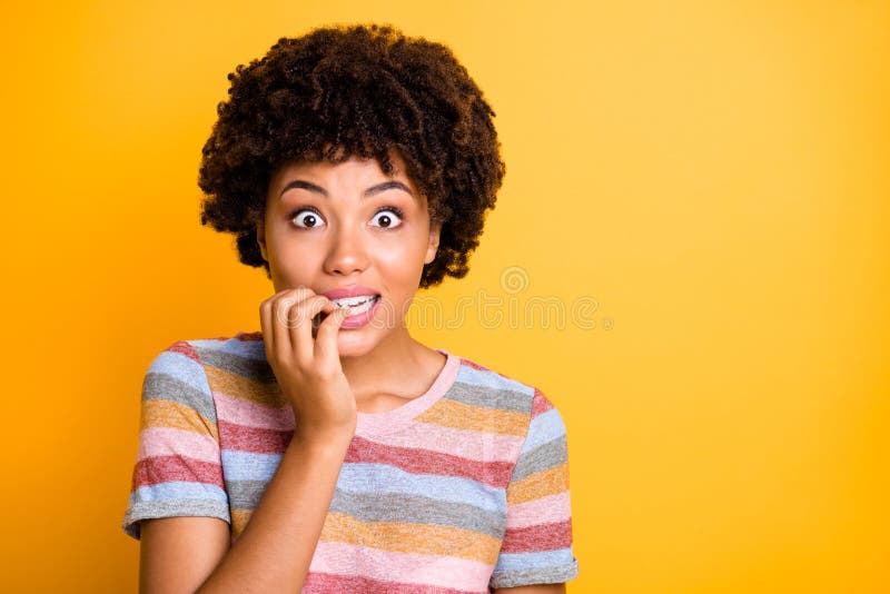 Photo of shocked impressed black girlfriend, biting her nails looking at sales she has not expected to see near empty space isolated over vivid yellow color background. Photo of shocked impressed black girlfriend, biting her nails looking at sales she has not expected to see near empty space isolated over vivid yellow color background