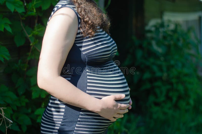 Foto De Una Mujer Embarazada Con Un Vestido a Rayas. Vista Lateral Del  Abdomen. En Perfil. Manos En El Estómago Imagen de archivo - Imagen de  morena, brillante: 188042387