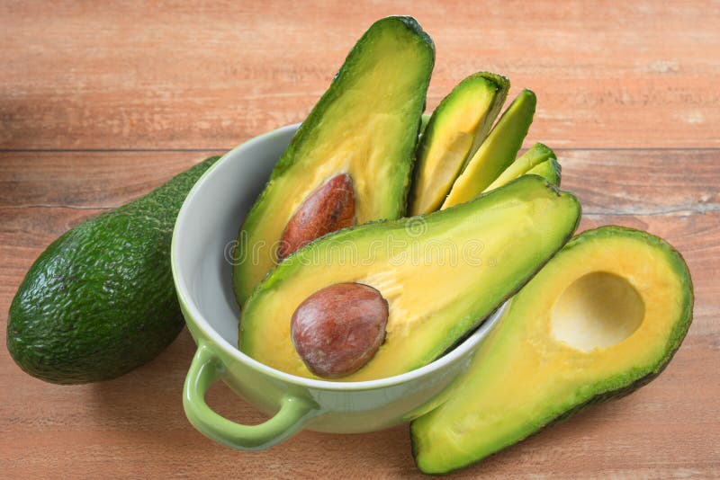 Foto del primo piano degli avocado affettati freschi, semi marroni visibili in ciotola verde su fondo di legno marrone immagine stock Foto del primo piano degli avocado affettati freschi, semi marroni visibili in ciotola verde su fondo di legno marrone immagine stock